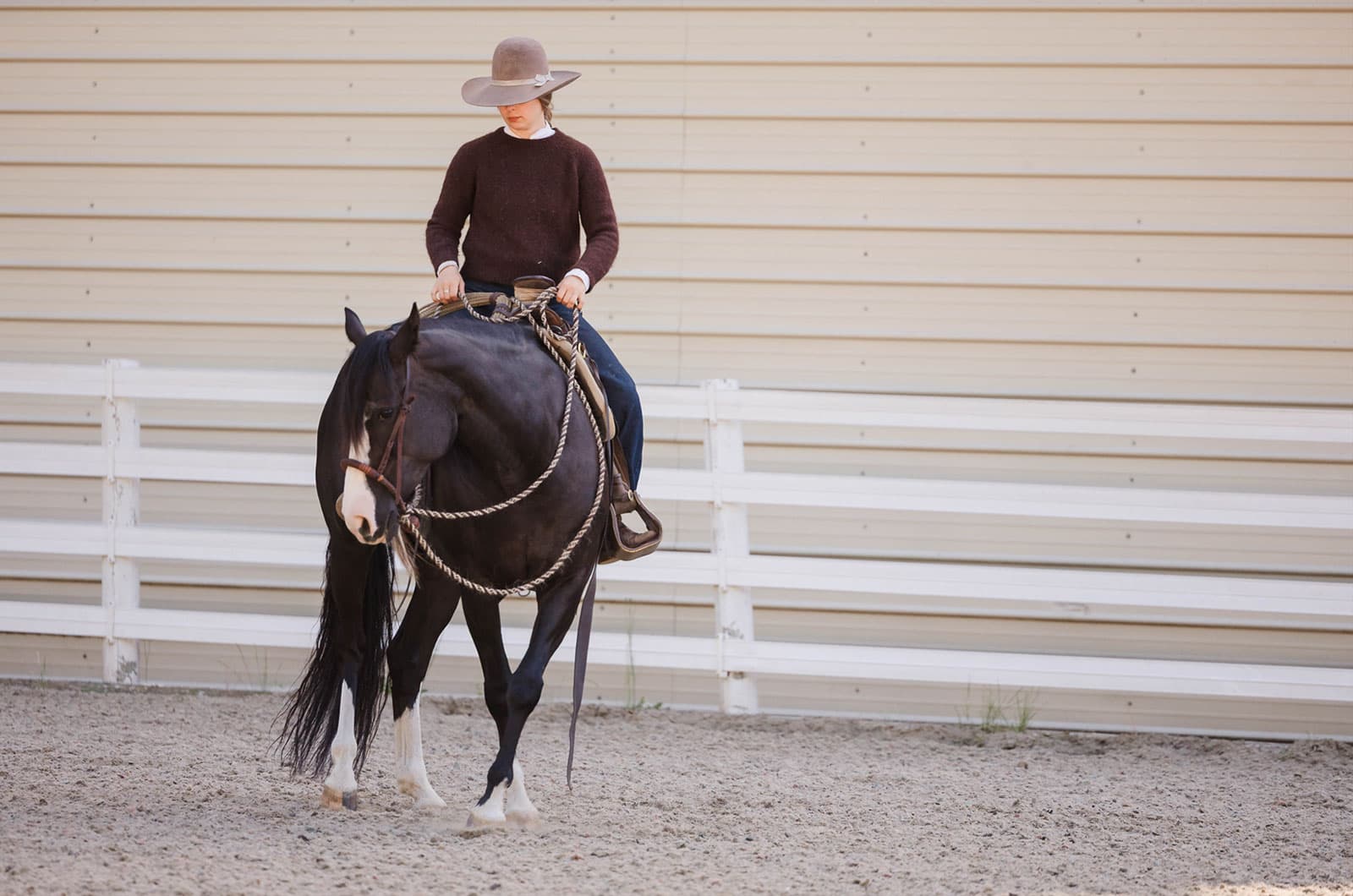 Lili rides along a white rail fence in the arena
